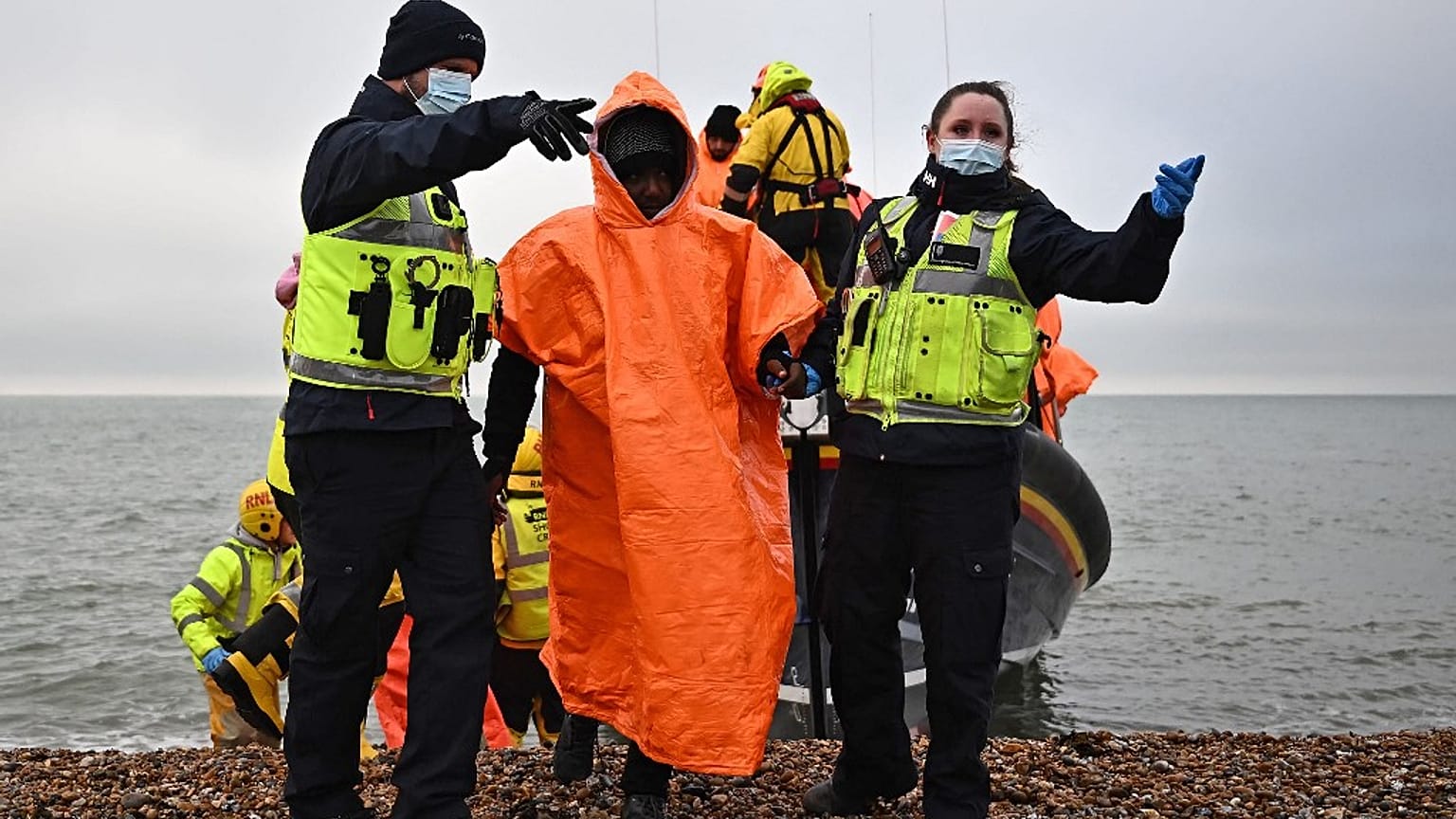 A cold migrant is escorted ashore after being picked up at sea.