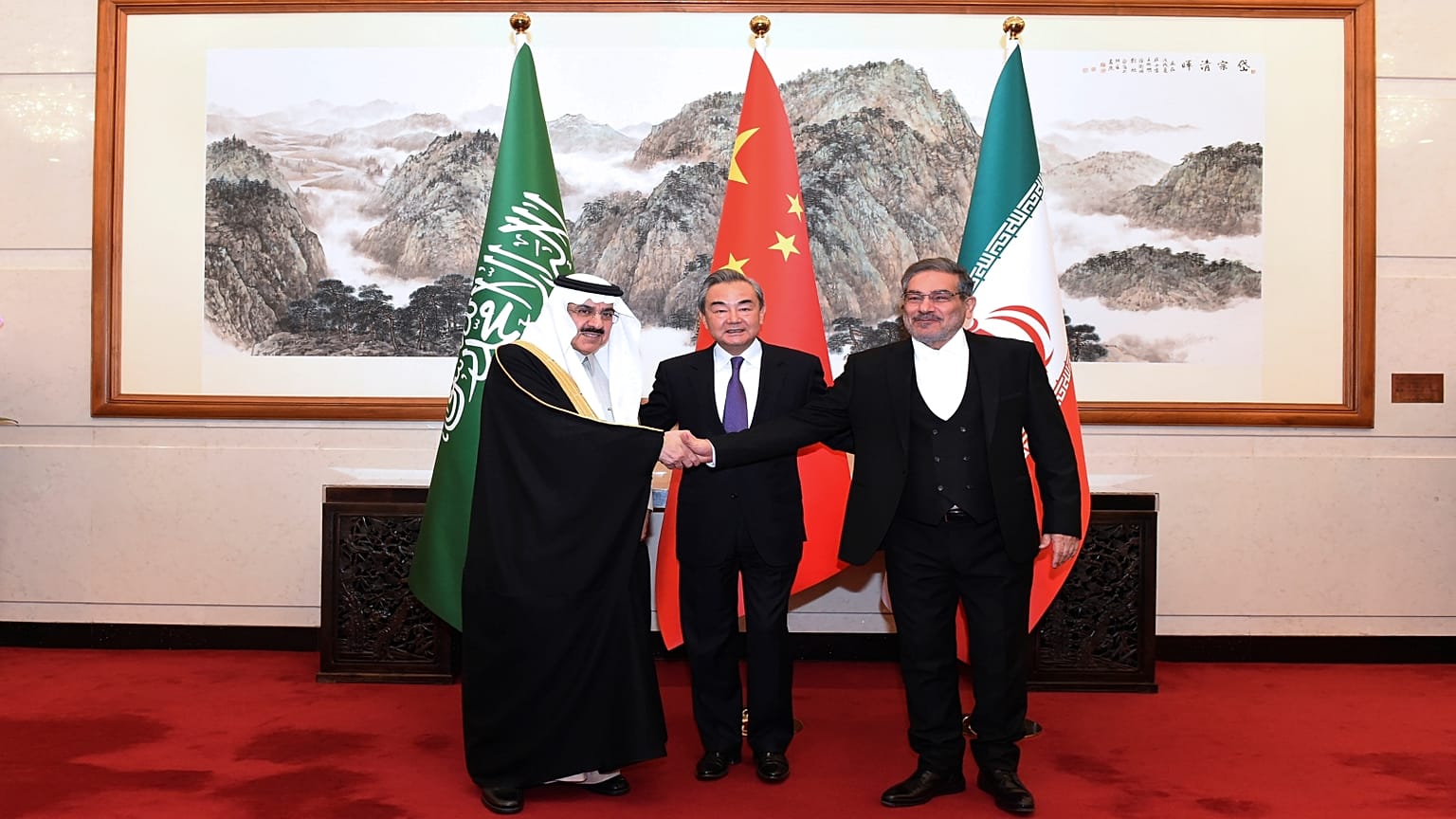 أمين المجلس الأعلى للأمن القومي الإيراني علي شمخاني (يمين) يصافح مستشار الأمن القومي السعودي مسعد بن محمد العيبان بوساطة صينية