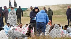 Rescued migrants sit covered in blankets at a beach near Cutro, southern Italy.