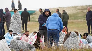 Rescued migrants sit covered in blankets at a beach near Cutro, southern Italy.