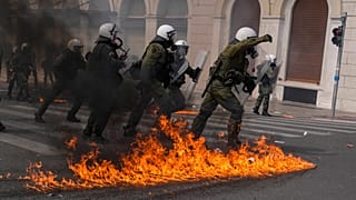 Riot police officers walk among flames of petrol bombs thrown by protestors during a protest in central Athens, Thursday, March 16, 2023. 