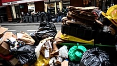 A man (top) walks past a pile of garbage bags that have been piling up since waste collectors went on strike. 15 March 2023