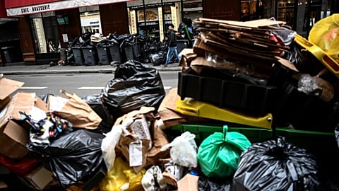 A man (top) walks past a pile of garbage bags that have been piling up since waste collectors went on strike. 15 March 2023