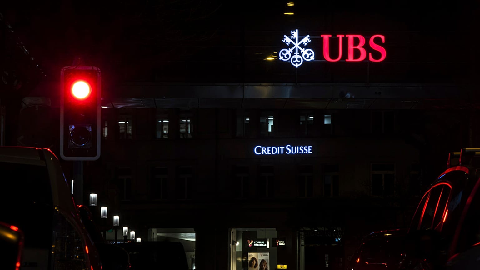 The illuminated logos of the Swiss banks Credit Suisse and UBS are seen on buildings next to traffic lights in Zurich, Switzerland