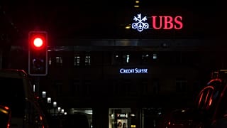 The illuminated logos of the Swiss banks Credit Suisse and UBS are seen on buildings next to traffic lights in Zurich, Switzerland