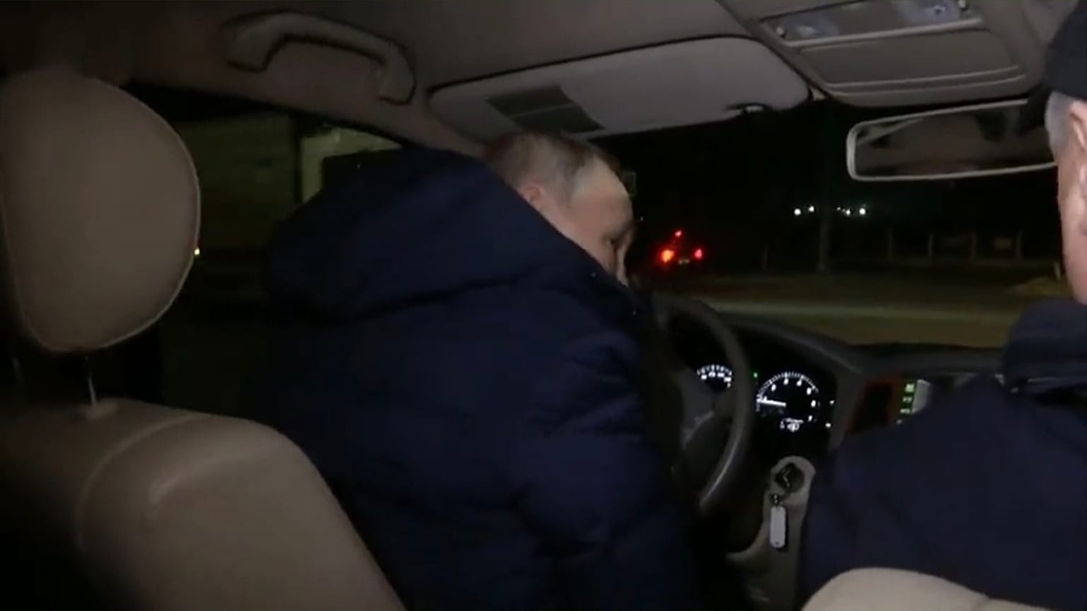 Vladimir Putin, di spalle, al volante di un'automobile per le strade di Mariupol.