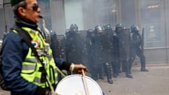 A protester wearing a yellow jacket plays drums in front of police officers during clashes at a demonstration against plans to push back France's retirement age in Paris