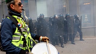 A protester wearing a yellow jacket plays drums in front of police officers during clashes at a demonstration against plans to push back France's retirement age in Paris