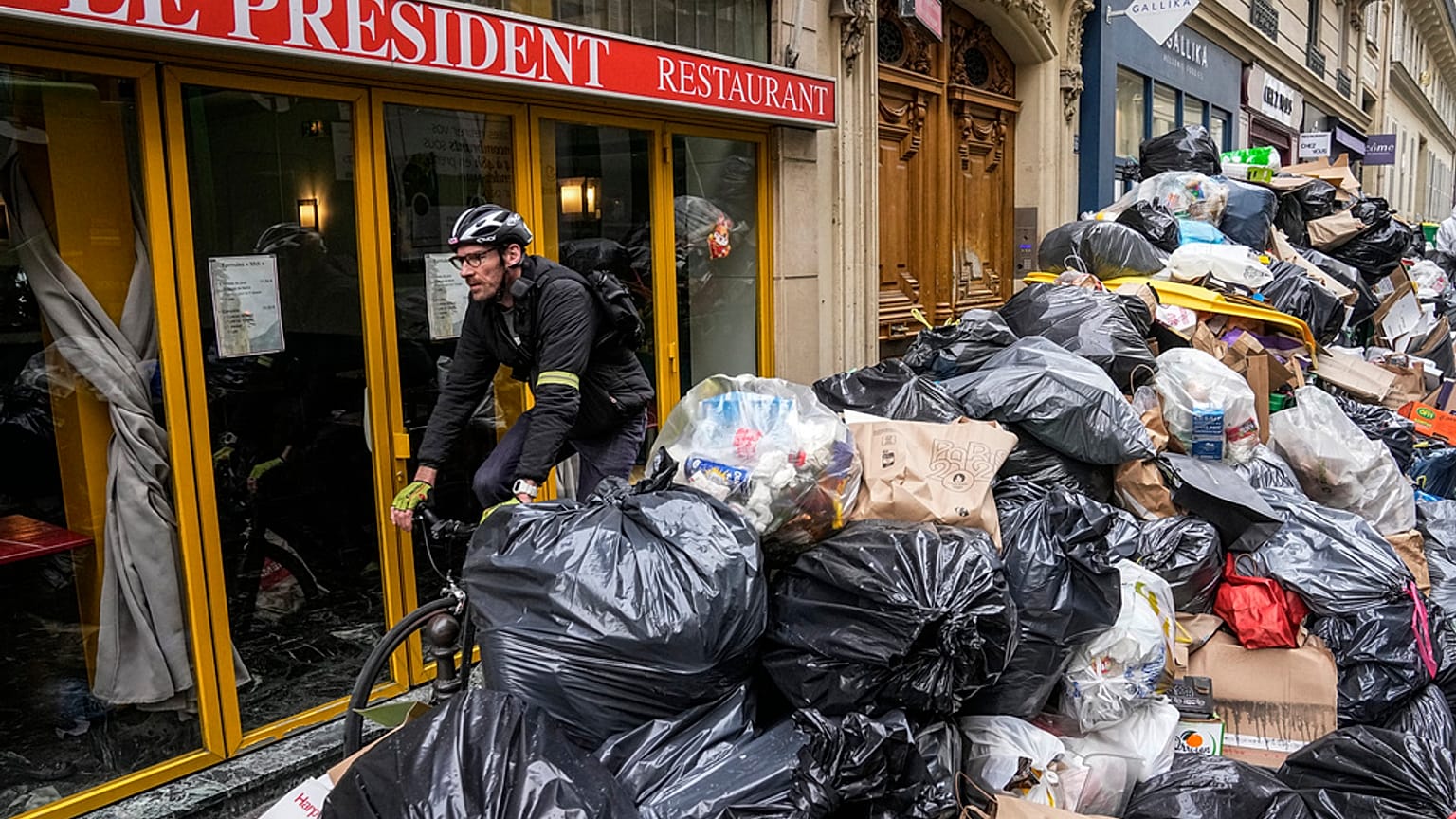 A cyclist rides past an uncollected garbage pile next to the cafe "The President" in Paris, Tuesday, March 21, 2023. 