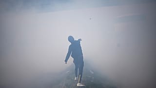 A protester covered in tear gas throws a rock at French police officers as he and oil workers block the access to an oil depot in Fos-sur-Mer, France, March, 21, 2023.