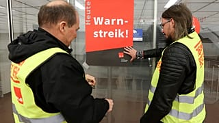 Union representatives stick a poster reading "Warning strike!" on a glass door at Hamburg Airport .