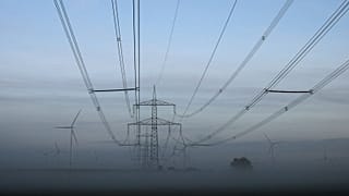 Wind turbines stand next to electricity pylons near Muencheberg, Germany.