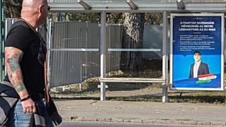 Egy kutyát sétáltató férfi egy Magyarország jobban teljesít plakát mellett a Városligetben, 2019-ben