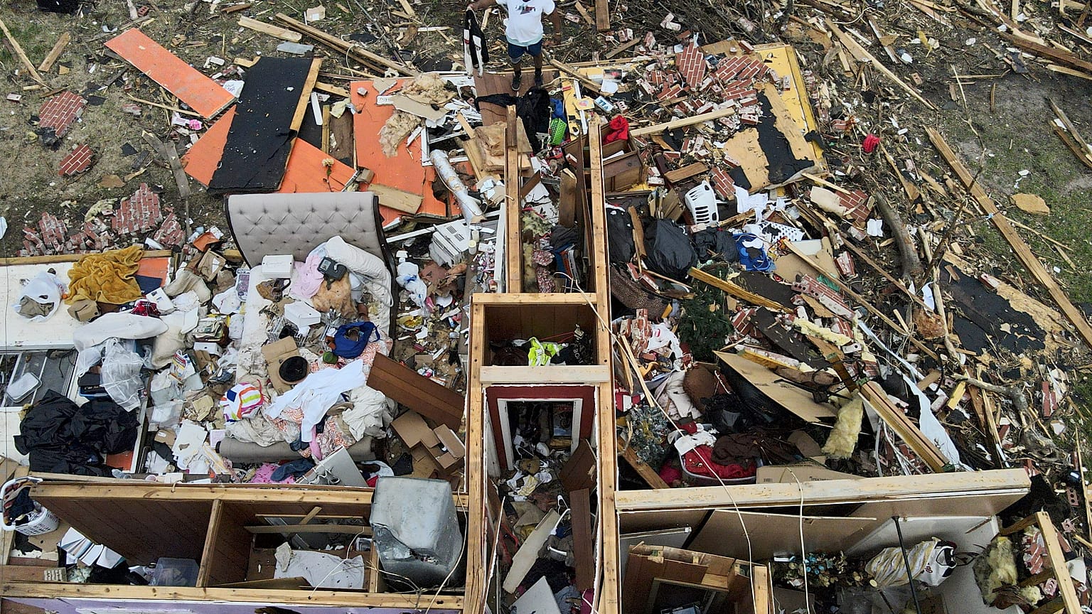 A man, top center, salvages a jacket as he looks over a tornado damaged home, Sunday, March 26, 2023, in Rolling Fork, Mississippi