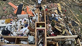 A man, top center, salvages a jacket as he looks over a tornado damaged home, Sunday, March 26, 2023, in Rolling Fork, Mississippi