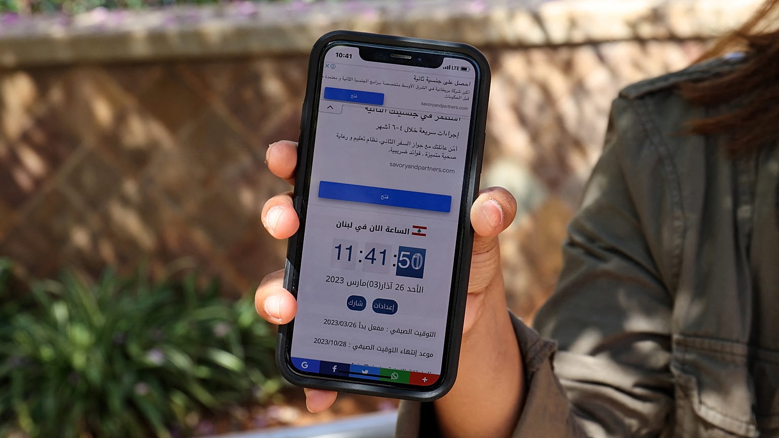 A woman in Beirut holds a mobile telephone showing contradicting time zones.