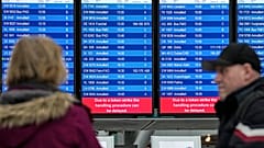 Passagiere vor einen Bildschirm mit gestrichenen Flügen am Flughafen in Düsseldorf. 27. März 2023