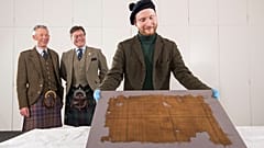 V&A Dundee curator James Wylie with the Glen Affric tartan, with STA's Peter MacDonald and John McLeish looking on