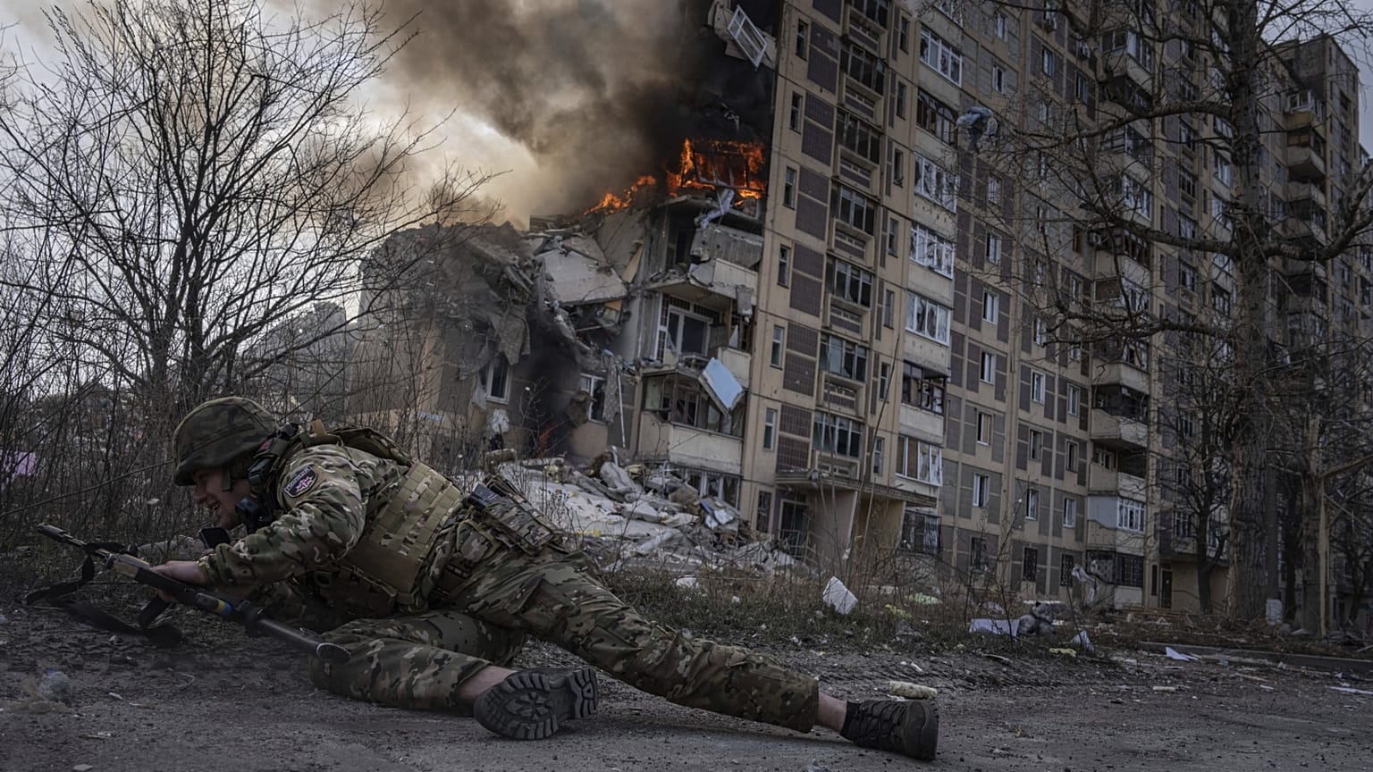 Ukrán rendőrtiszt fedezéket keres egy égő ház előtt Avdijivkában