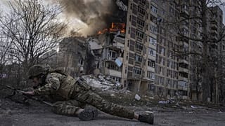 Ukrán rendőrtiszt fedezéket keres egy égő ház előtt Avdijivkában
