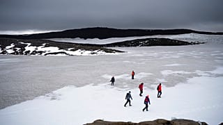 People walk on snow atop the Ok volcano crater on their way to a ceremony by the area which once was the Okjokull glacier