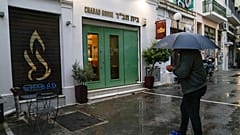 A man holding an umbrella stands in front of a Jewish restaurant that Greek officials believe was one of the targets of a planned terrorist attack, in central Athens, March 28