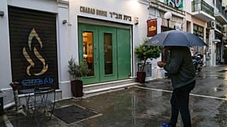 A man holding an umbrella stands in front of a Jewish restaurant that Greek officials believe was one of the targets of a planned terrorist attack, in central Athens, March 28