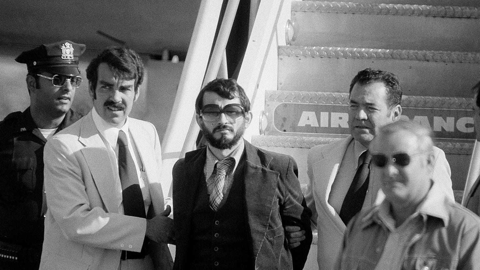 Zvonko Busic, com barba, é conduzido de um avião sob custódia policial no Aeroporto Kennedy, Nova Iorque, depois de ter sido preso por pirataria aérea. 12 de Setembro de 1976