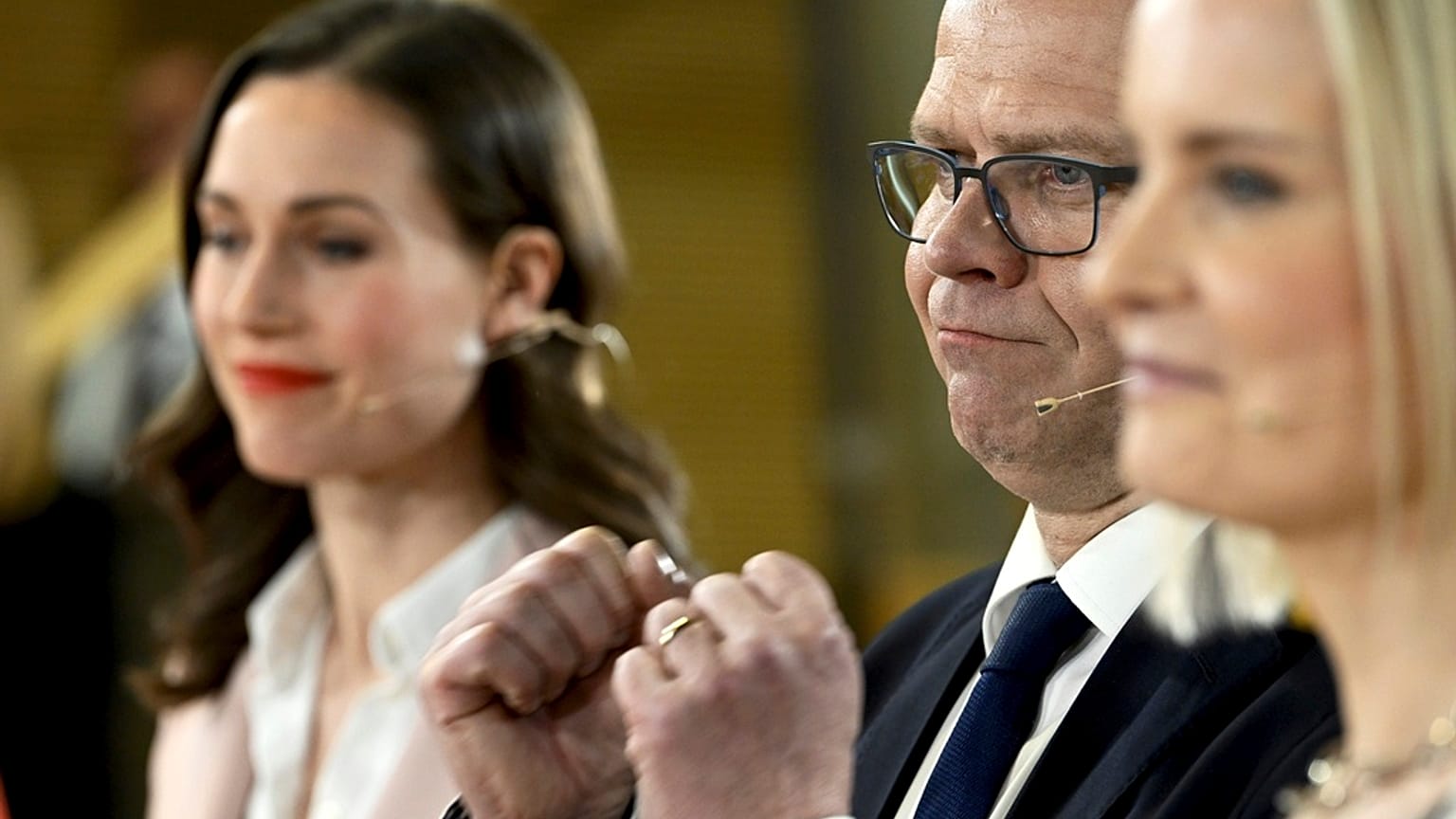 Chair of SDP Sanna Marin, left, and chair of The Finns party Riikka Purra, right, look on as National Coalition Party chair Petteri Orpo cheers at the parliamentary election.