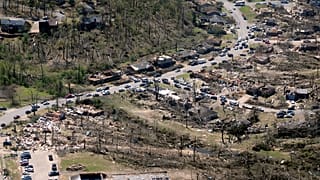 Cars line up along the road as cleanup continues from Friday's tornado damage,