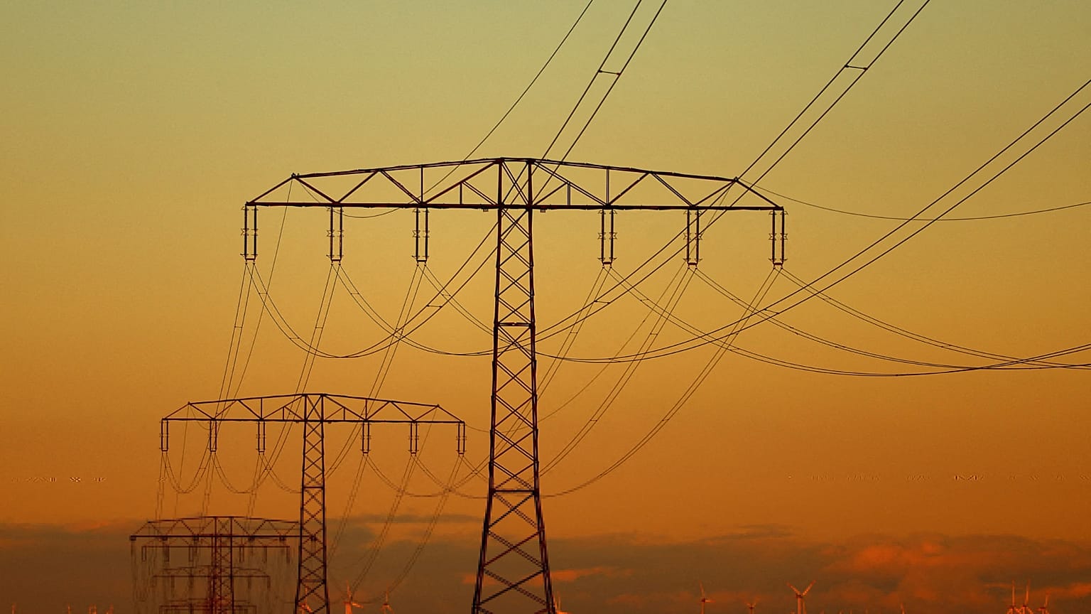 Electrical power pylons with high-voltage power lines are seen in front of wind turbines during sunset near Weselitz, Germany.