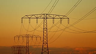 Electrical power pylons with high-voltage power lines are seen in front of wind turbines during sunset near Weselitz, Germany.