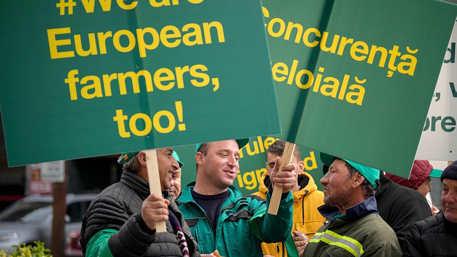 Men talk as they hold banners during a farmers' protest in front of the Representative Office of the European Commission in Bucharest, Romania, Friday, April 7, 2023. 