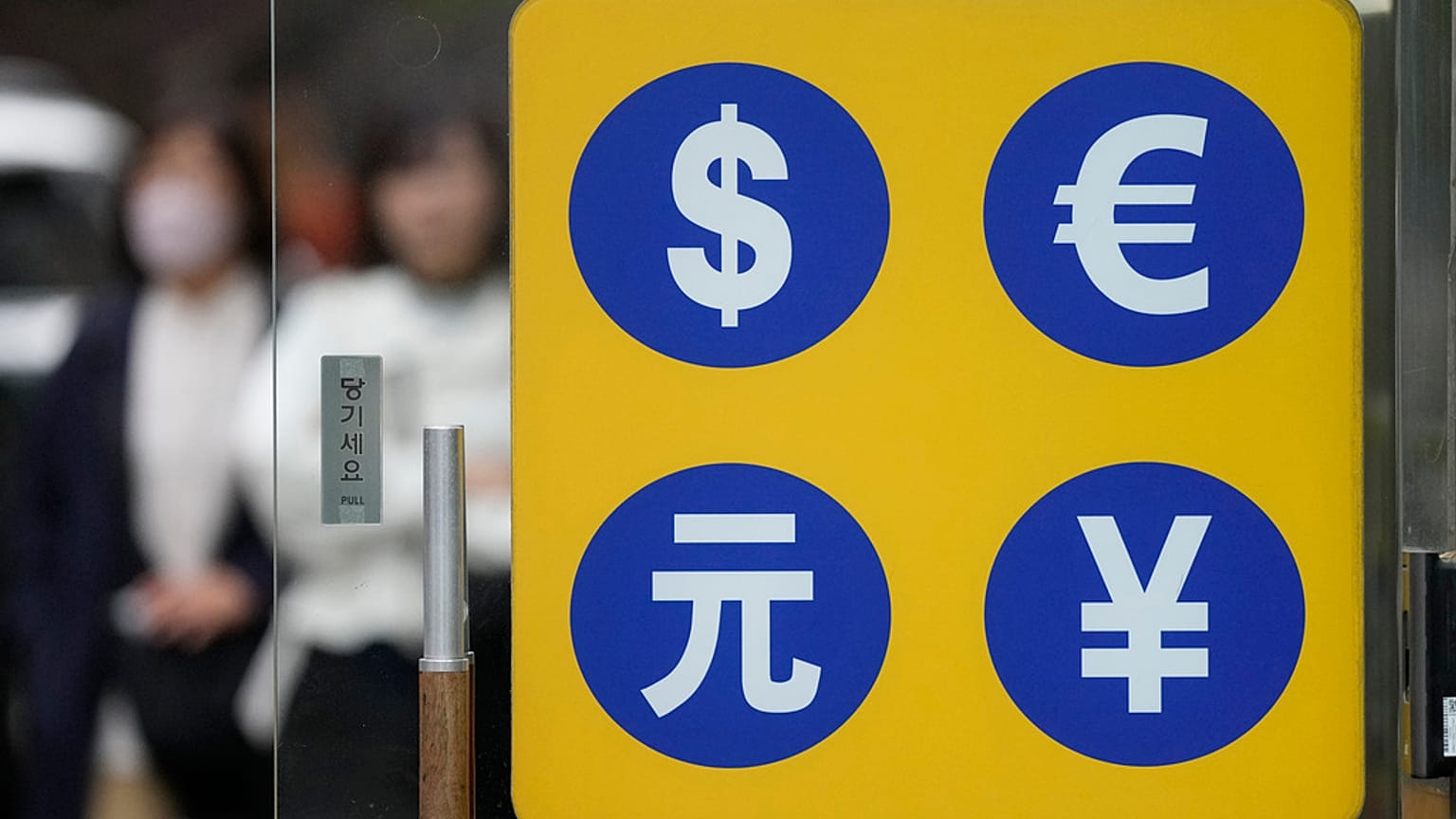 People walk near a sign of foreign currency outside a money exchange office at a shopping district in Seoul, South Korea, Tuesday, April 11, 2023. 