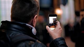 Image shows a man using the Be My Eyes app, which connects low-vision users to sighted volunteers via video call to act as their eyes.