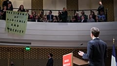 Der französische Präsident Emmanuel Macron und Demonstranten, die während eines Vortrags ein Transparent mit der Aufschrift "Präsident der Gewalt und der Heuchelei" entfalten