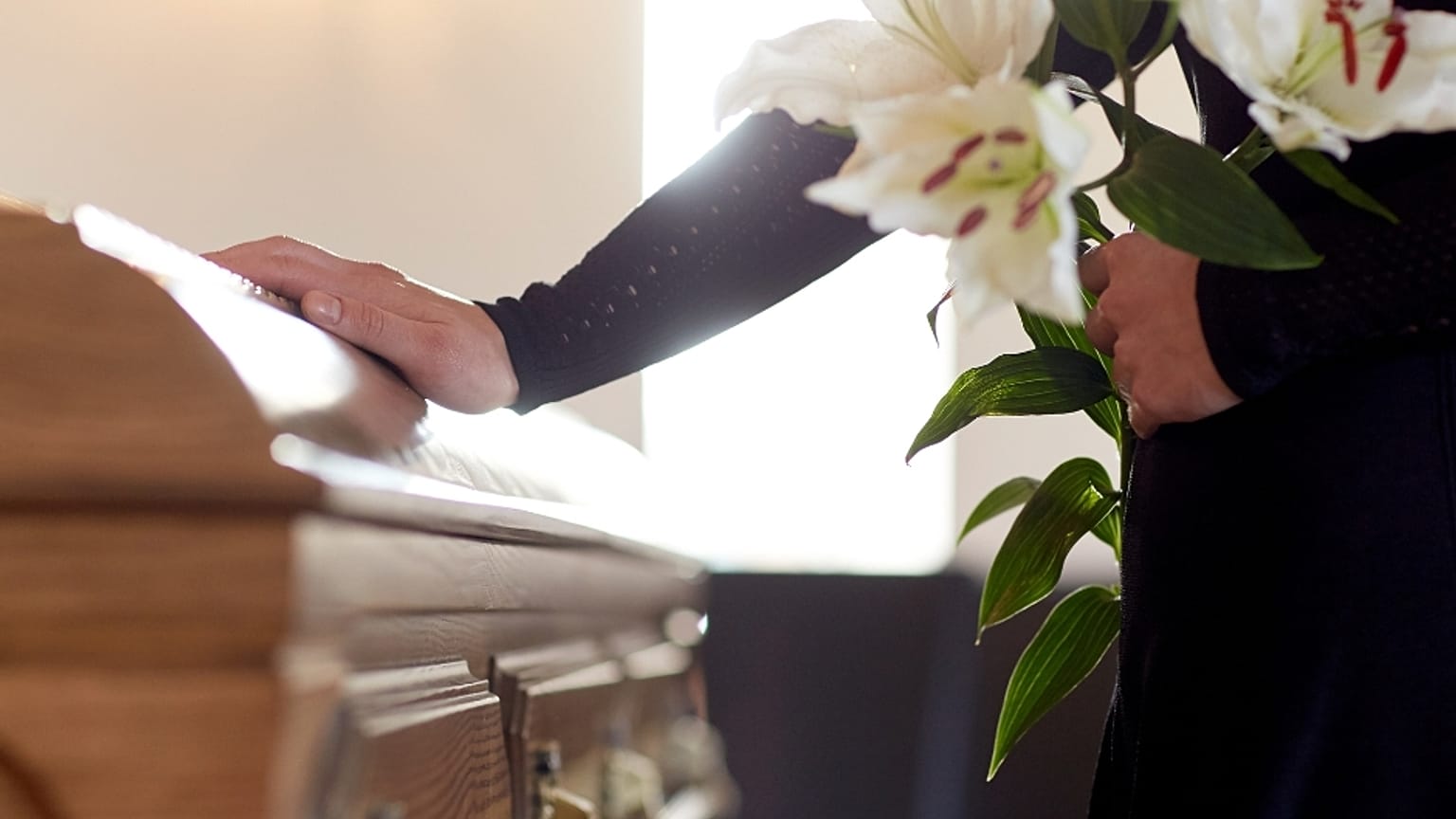 A man stands sadly by a coffin. 