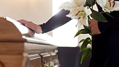A man stands sadly by a coffin. 