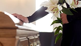 A man stands sadly by a coffin. 