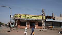 People walk past shuttered shops in Khartoum, Sudan, Tuesday, April 18, 2023. 