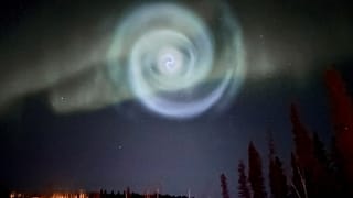 A light baby blue spiral resembling a galaxy appears amid the aurora for a few minutes in the Alaska skies
