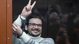 Russian opposition activist Ilya Yashin gestures, smiling, as he stands in a defendant's cubicle prior to his original sentencing in December 2022.