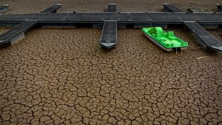 A green pedal boat is tied to a dock in a dried part of the Sau reservoir.