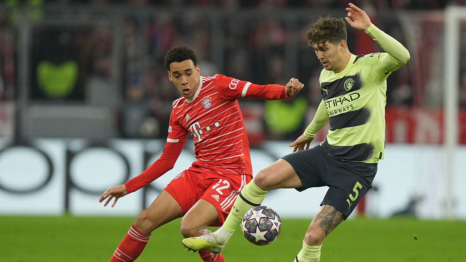 John Stones (Manchester City, sárgában) és Jamal Musiala, a Bayern München játékosa harcol a labdáért a müncheni Allianz Arénában 2023. április 19-én.