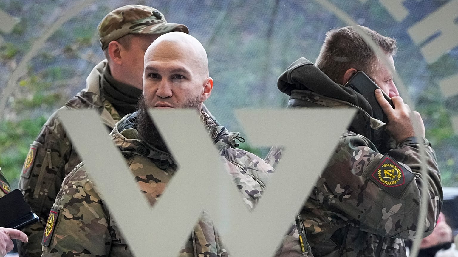 Visitors wearing military camouflage stand at the entrance of the 'PMC Wagner Centre'. 