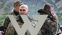 Visitors wearing military camouflage stand at the entrance of the 'PMC Wagner Centre'. 