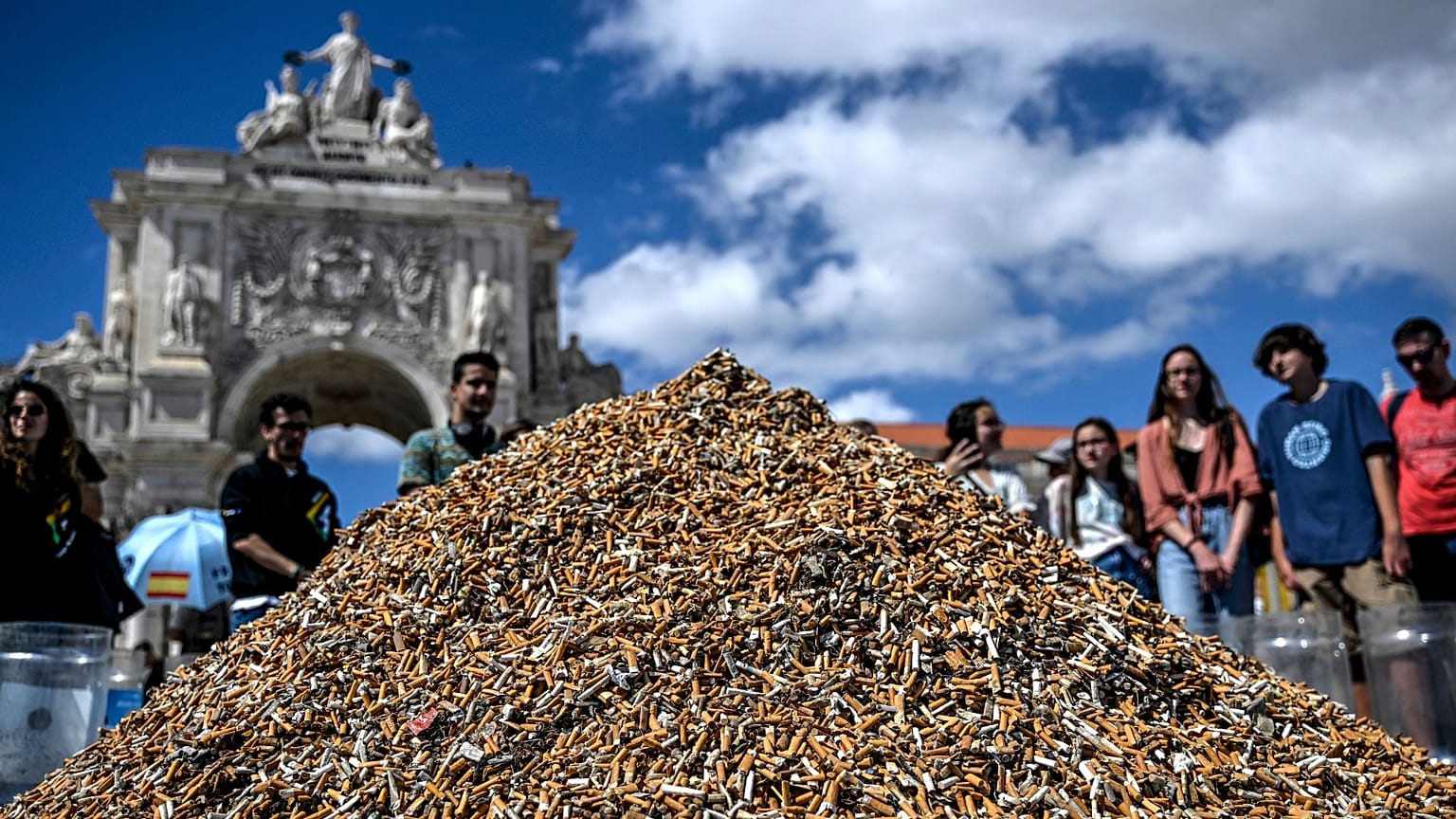 People look at a pile of cigarette butts, collected in one week, at Comercio Square in Lisbon on April 23, 2023. 