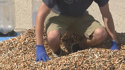 Andreas Noe, militant écologiste allemand, sur une pile de mégots de cigarettes collectés en une semaine, à Lisbonne, le 24 avril 2023.
