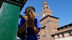 Mulher a beber água numa fonte pública no Castelo Sforza em Milão, Itália
