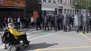 Ein Rollstuhlfahrer steht bei einer Demonstration im französischen Lille Einsatzkräften gegenüber (Aufnahme vom 13. April 23)
